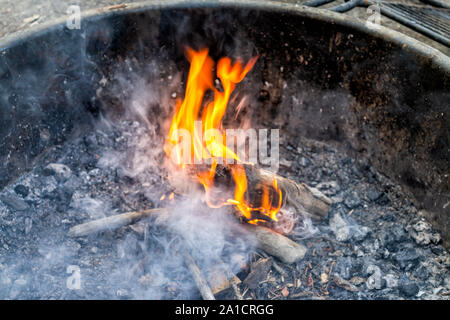 Closeup of wooden logs wood on large fire burning long exposure of red orange flame at campground campfire grill in outdoor park in evening and smoke Stock Photo