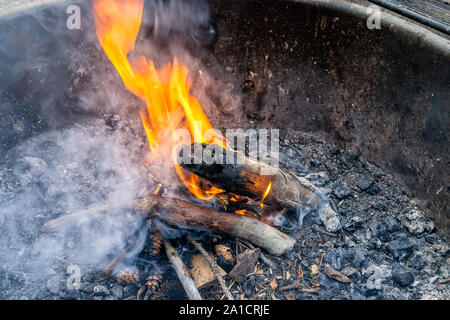 Closeup of smoke at wooden logs wood on large fire burning long exposure of red orange flame at campground campfire grill in outdoor park in evening Stock Photo