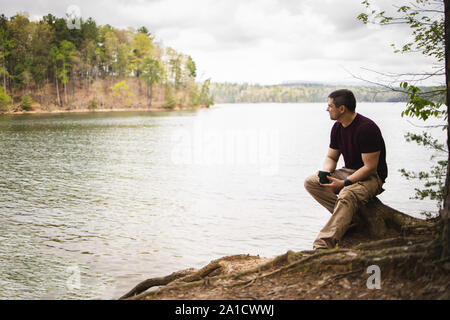 Mid aged caucasian man is sitting by the lake with a cup of coffee Stock Photo
