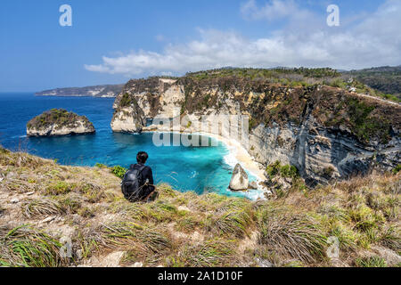Aerial view of travel people with backpack and in shorts on the ocean, cliffs and tropical beach background. Atuh beach, Nusa Penida, Indonesia. Stock Photo