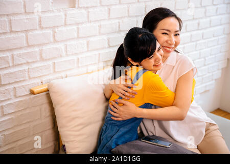 Loving smiling Asian women hugging happily while sitting together on couch at living room Stock Photo