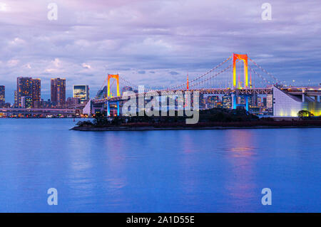 Odaiba Rainbow bridge with illuminated colourful light and Tokyo bay view in twilight cityscape in background under pinkish sky Stock Photo