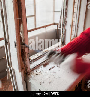 installer in red sweater using crowbar dismantles old window frame and sill Stock Photo