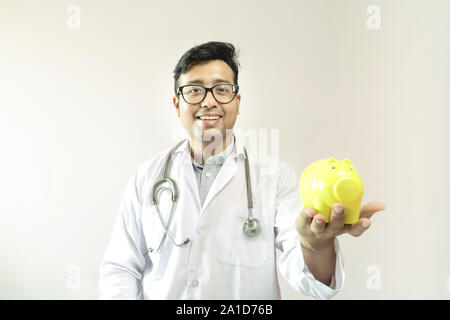 male indian doctor in white coat and stethoscope with a yellow piggy bank Stock Photo