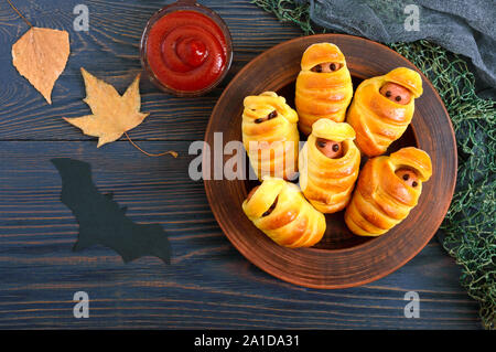 Funny sausage mummies in dough with ketchup on table. Halloween food. Top view. Flat lay Stock Photo