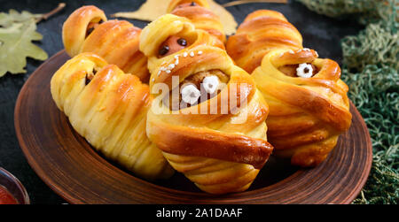 Funny sausage and cutlets mummies in dough with eyes, ketchup on table. Halloween food. Stock Photo