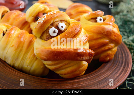 Funny sausage and cutlets mummies in dough with eyes, ketchup on table. Halloween food. Close up Stock Photo