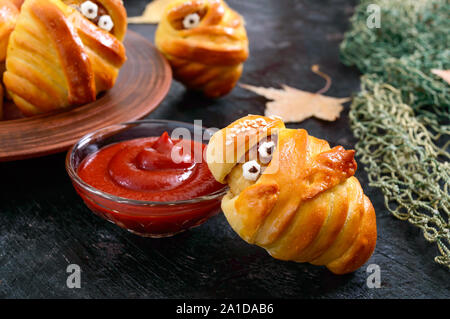 Funny sausage and cutlets mummies in dough with eyes, ketchup on table. Halloween food. Stock Photo