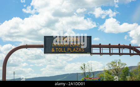 Pennsylvania highway, USA. May 6, 2019: Slow down in work zones and toll plazas Warning led road sign billboard on a highway, cloudy blue sky Stock Photo