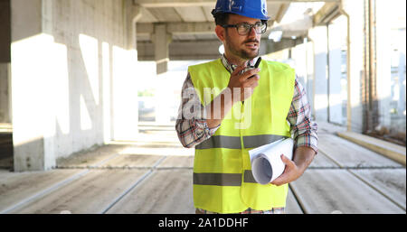 Male architect with blueprints using walkie-talkie Stock Photo
