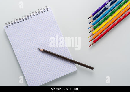 Clean notepad in a cage with a pencil lying on it and color pencils in the form of an arrow on a white background top view Stock Photo