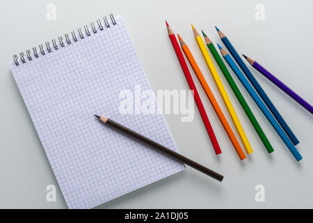 Clean notepad in a cage with a pencil lying on it and rainbow color pencils on a white background top view Stock Photo