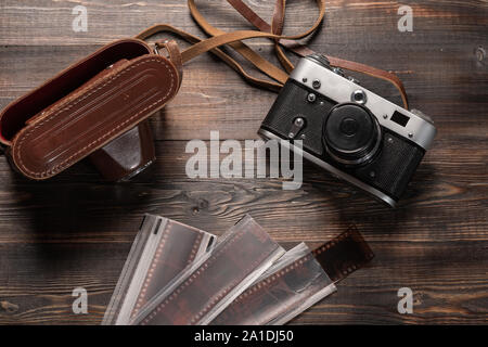 Vintage film camera with leather case and photographic film on dark wooden table. The view from the top Stock Photo
