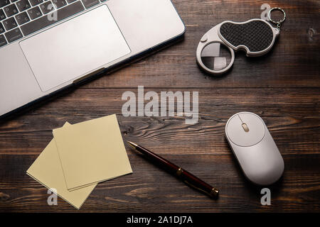 Laptop, opened magnifier, mouse, pen and paper for taking notes on the dark wooden table. Close up for your text Stock Photo