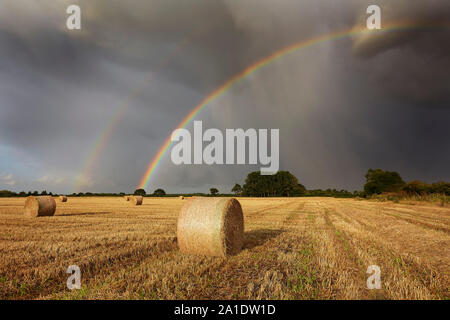 Double rainbow in a harvested field of stubble and straw bales, East Yorkshire, UK Stock Photo