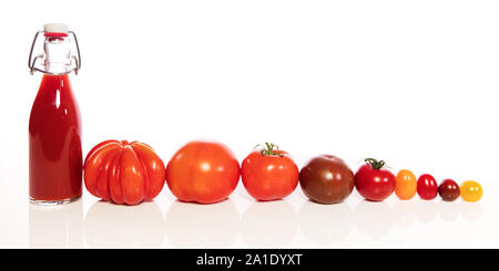 various tomatoes and a bottle with juice in a row, in front of white Stock Photo