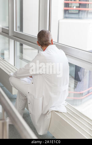 male doctor is having a break, looking thoughtful out of the window Stock Photo