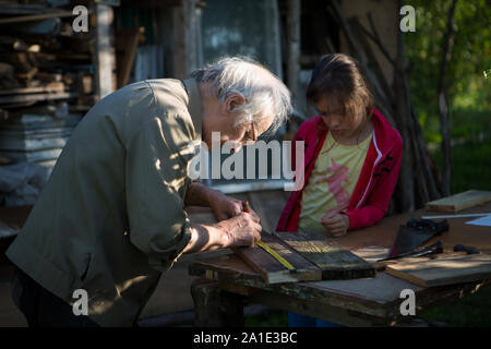 Elderly man with a girl make a birdhouse in the country Stock Photo