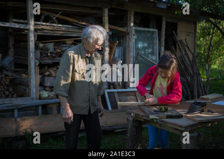 Elderly man with a girl make a birdhouse in the country Stock Photo