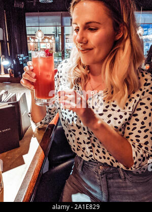 Woman in her twenties wearing dalmatian print shirt at a bar, drinking a cocktail Stock Photo