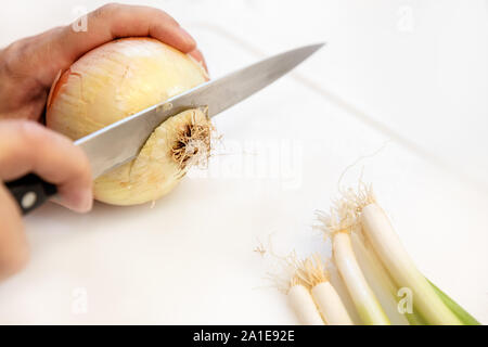 Man is cutting a fresh onion and escallion on white chopping board Stock Photo