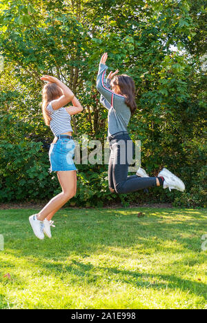 Two teenagers girls jumping in a park in summertime. Having fun in holidays. Happy friends spending time together. Friendship. Stock Photo