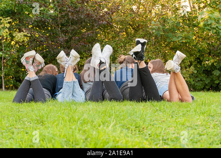 View of the legs and shoes of a gang of young teenagers girls standing on the grass of a park. Having fun outdoors in summertime. Enjoying the holiday Stock Photo