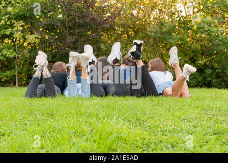 View of the legs and shoes of a gang of young teenagers girls standing on the grass of a park. Having fun outdoors in summertime. Enjoying the holiday Stock Photo