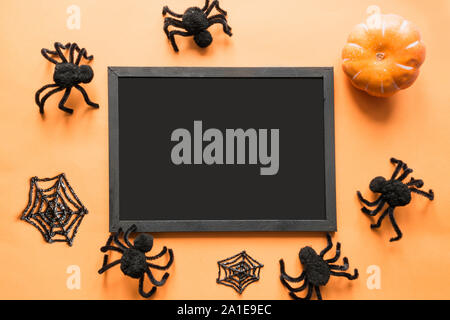 Halloween holiday blank with party decor, black spiders, web on orange. Flat lay, top view. Space for text. Stock Photo