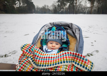 A caucasian baby boy aged between 4 and 5 months old with blue eyes in a pushchair in winter covered by a crochet blanket wearing a woollen hat Stock Photo