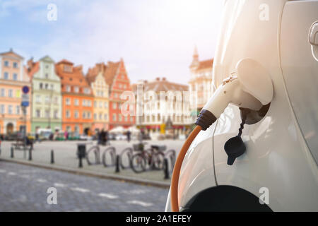 Close up of electric car with a connected charging cable on the blurred background of European city Stock Photo