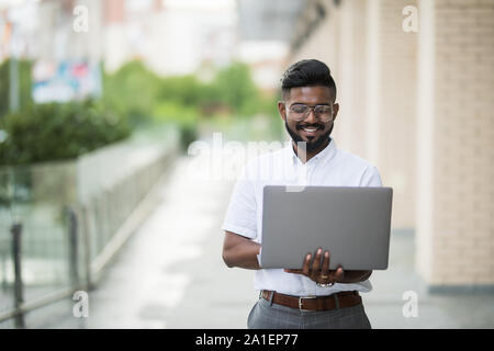 East Indian American College Student sits on stairs on campus, works on laptop computer. Stock Photo
