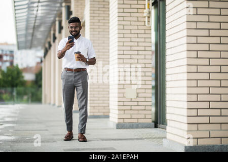 Positive indu student in casual wear watching funny video and messaging with friends in online chat on mobile phone using 4G internet connection stand Stock Photo