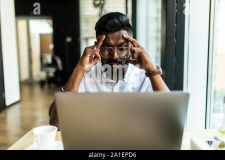 Young Asian businessman suffering from tired eyes after long hours of using laptop. Stock Photo