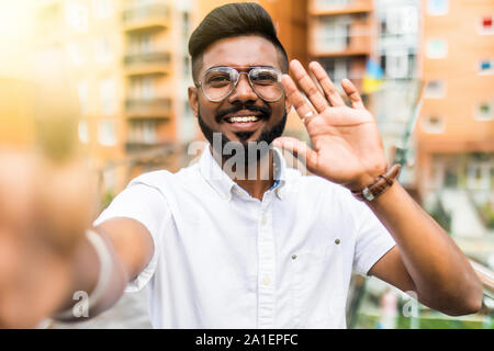 Smiling young guy taking selfie photo on smartphone on the street. Indian man using digital device. Stock Photo