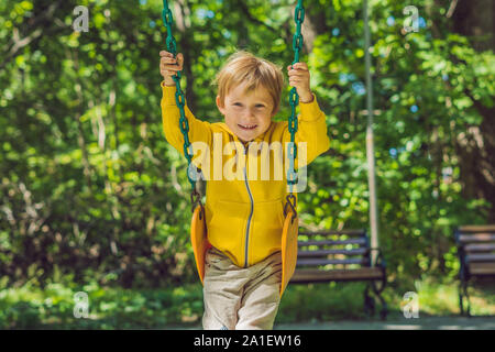 A boy in a yellow sweatshirt sits on a swing on a playground in autumn. Stock Photo