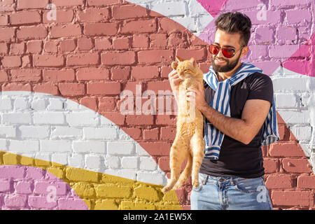 Pet owner and friendship concept - Handsome man is holding and hugging cute ginger cat. Cat with curious expression. Stock Photo