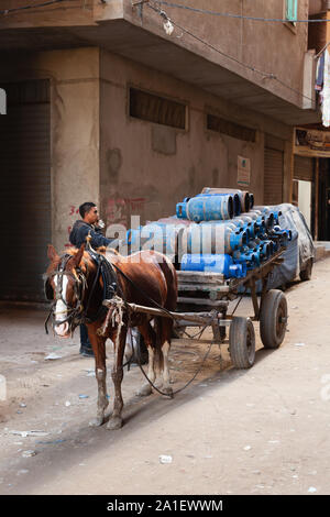 Alexandria, Egypt - December 18, 2018: Horse drawn cart full of blue gasbags, coachman stands nearby on a dirty street of Alexandria Stock Photo