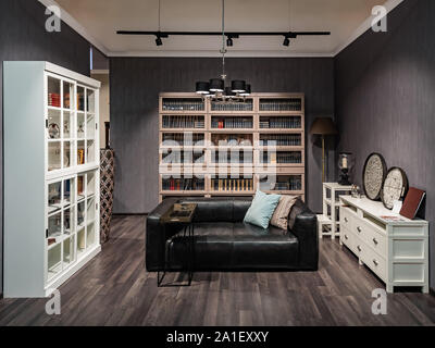 Living room interior with bookcase, cupboard, leather sofa, coffee table, chest of drawers and whatnot pendant light with spots on the ceiling Stock Photo