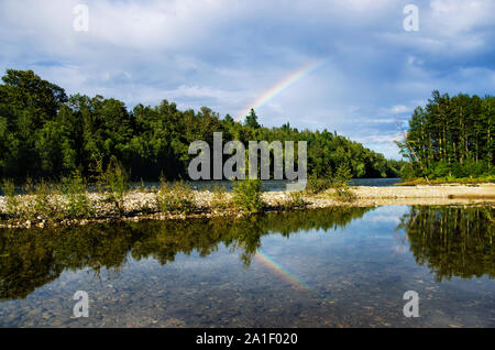 Rainbow over a lake reflected in the water in summer cloudy day Stock Photo
