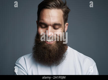 Smiling young man with a long beard wearing a t shirt standing alone against a gray background Stock Photo