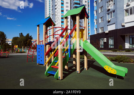 Empty colorful wooden children's slide with ladder on the playground. Attraction located in the yard against high-rise building and blue sky. Stock Photo