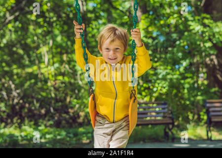 A boy in a yellow sweatshirt sits on a swing on a playground in autumn. Stock Photo