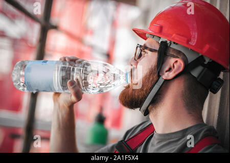 Construction mason worker sitting high on the scaffolding, resting and drinking water Stock Photo