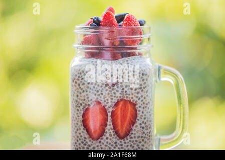 Healthy layered dessert with chia pudding, strawberry and honeysuckle in a mason jar on background of greenery. Stock Photo