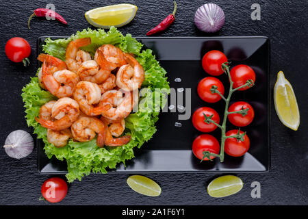 tasty grilled shrimps with tomato, chili and garlic with lime on black background