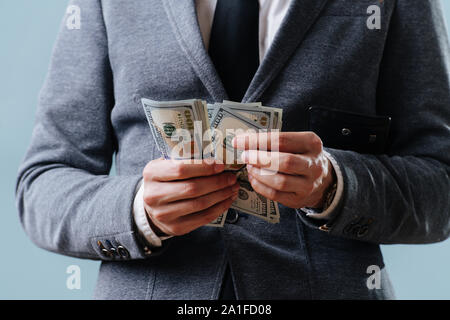 Businessman in a suit is counting cash one banknote after another over blue Stock Photo