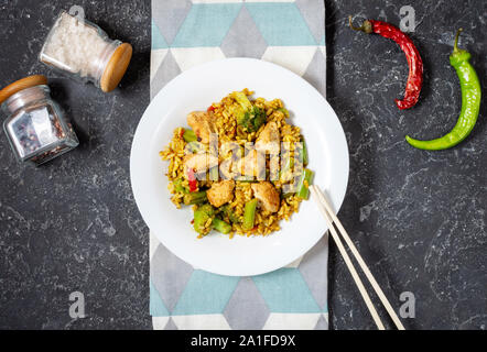 Rice with chicken meat and vegetables in a plate on black stone table. Top view Stock Photo