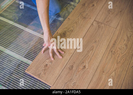 Man installing new wooden laminate flooring on a warm film floor. infrared floor heating system under laminate floor Stock Photo