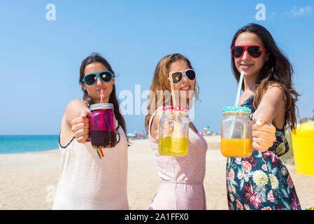 friendship and leisure concept - group of happy young women or female friends toasting non alcoholic drinks on summer beach Stock Photo